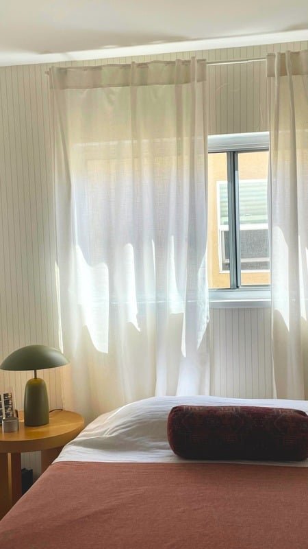 Liza's LA bedroom with sheer curtains, warm bedding, and a bedside lamp